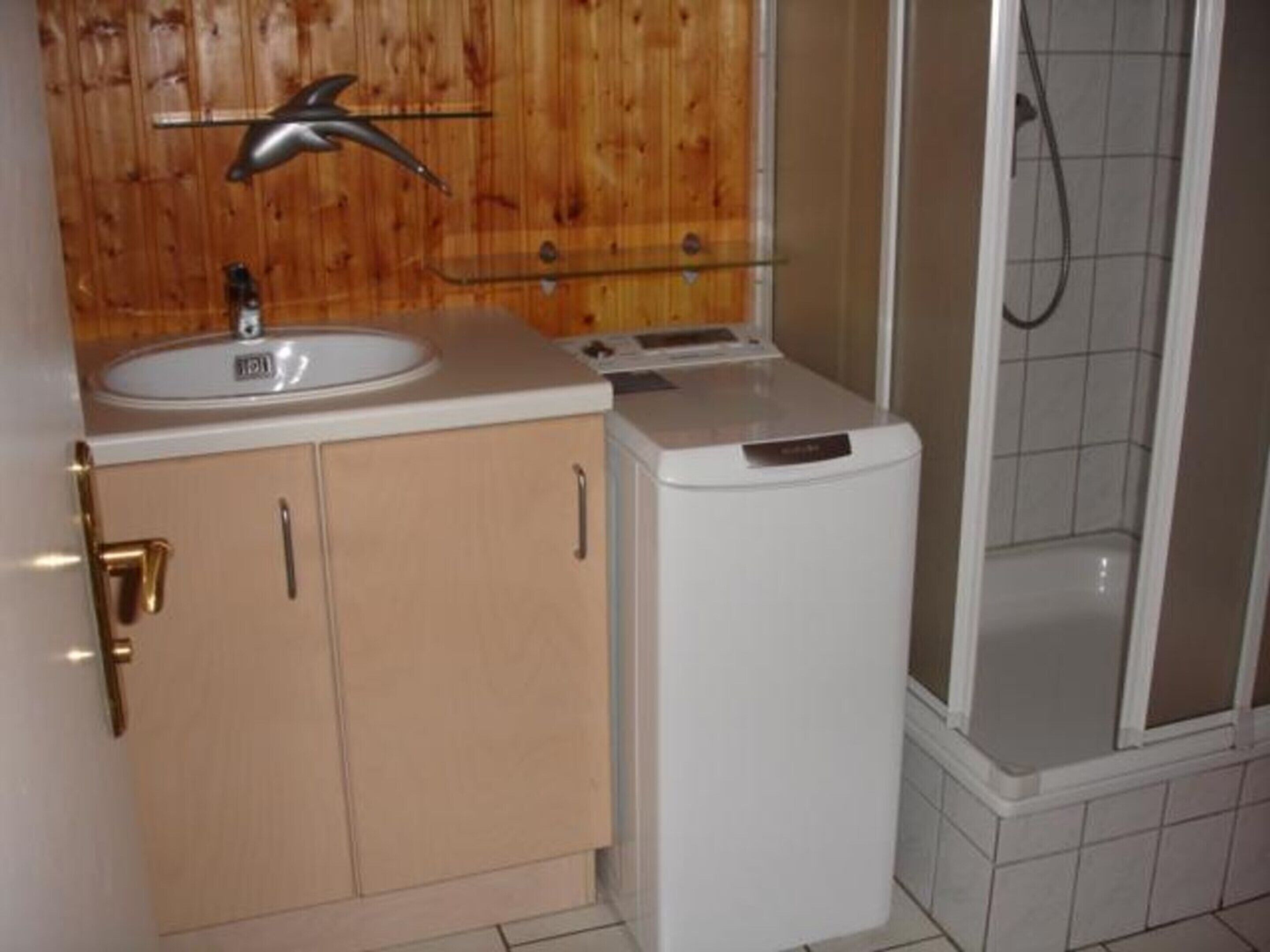 Ein Badezimmer mit einem Holzkosmetikschrank, einem Waschbecken, einem Spiegel und einer Duschkabine.
