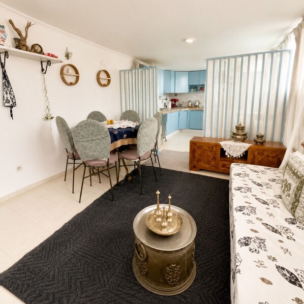 A living room with a dining area, a kitchen in the background, and a sofa with a patterned cover.