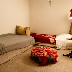 Ein Schlafzimmer mit einem Bett, einem kleinen runden Hocker, einer Lampe und einer Wandleuchte.