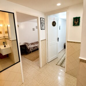 A hotel room with a bathroom, a bed with a patterned bedspread, a door with a decorative sign, and a small rug on the floor.