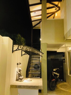 Un escalier avec une rampe en métal, une petite statue et une moto garée dans un espace abrité.