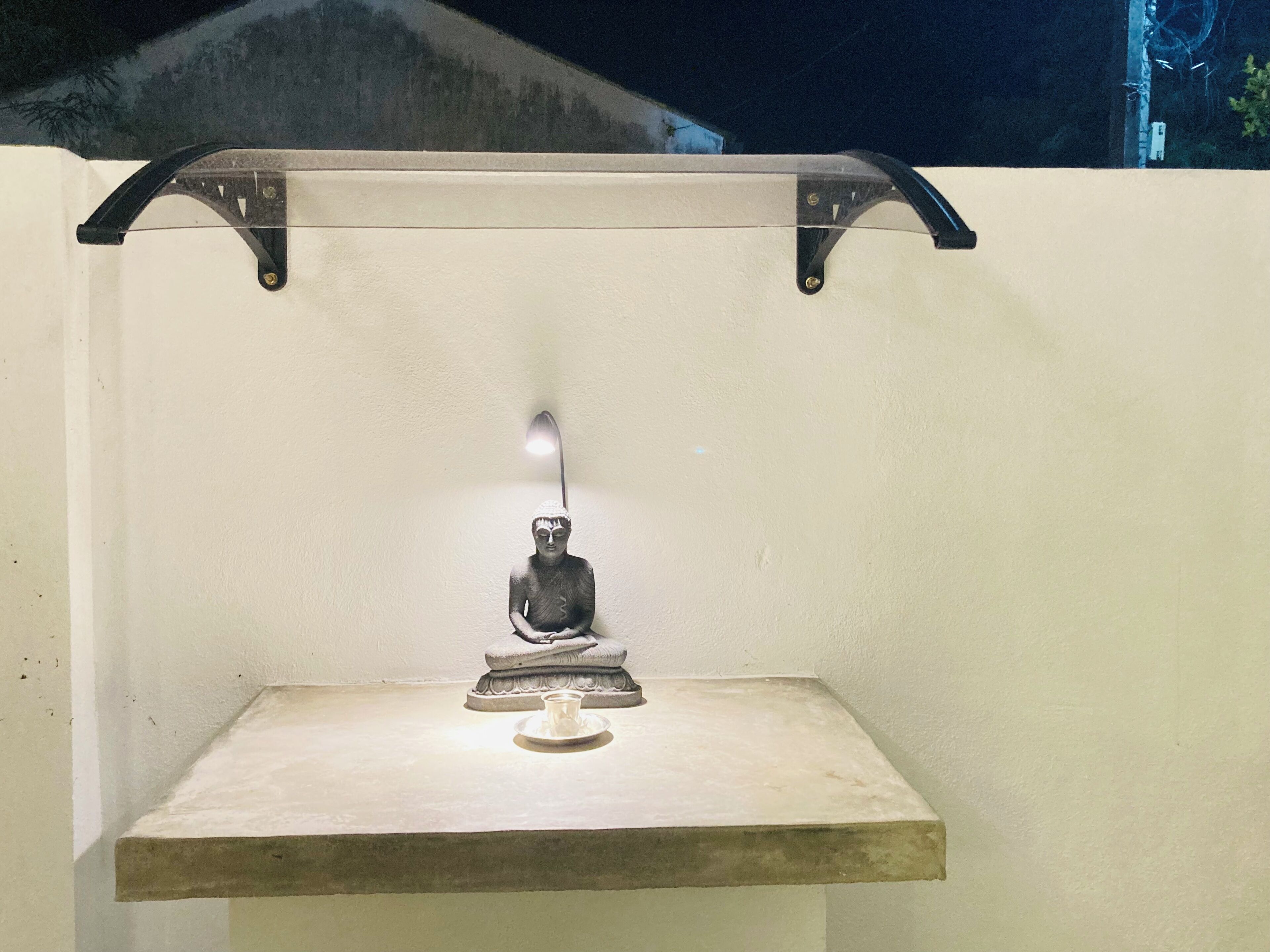 A statue on a platform with a light above it, mounted on a wall.