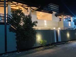 Un immeuble de deux étages doté d’un balcon, d’un petit arbre et d’une entrée fermée par un portail.