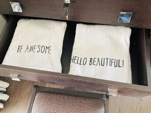 Un tiroir contenant deux serviettes, l’une avec l’inscription « SOYEZ GÉNIAL » et l’autre avec l’inscription « BONJOUR, BEAUTÉ ! »