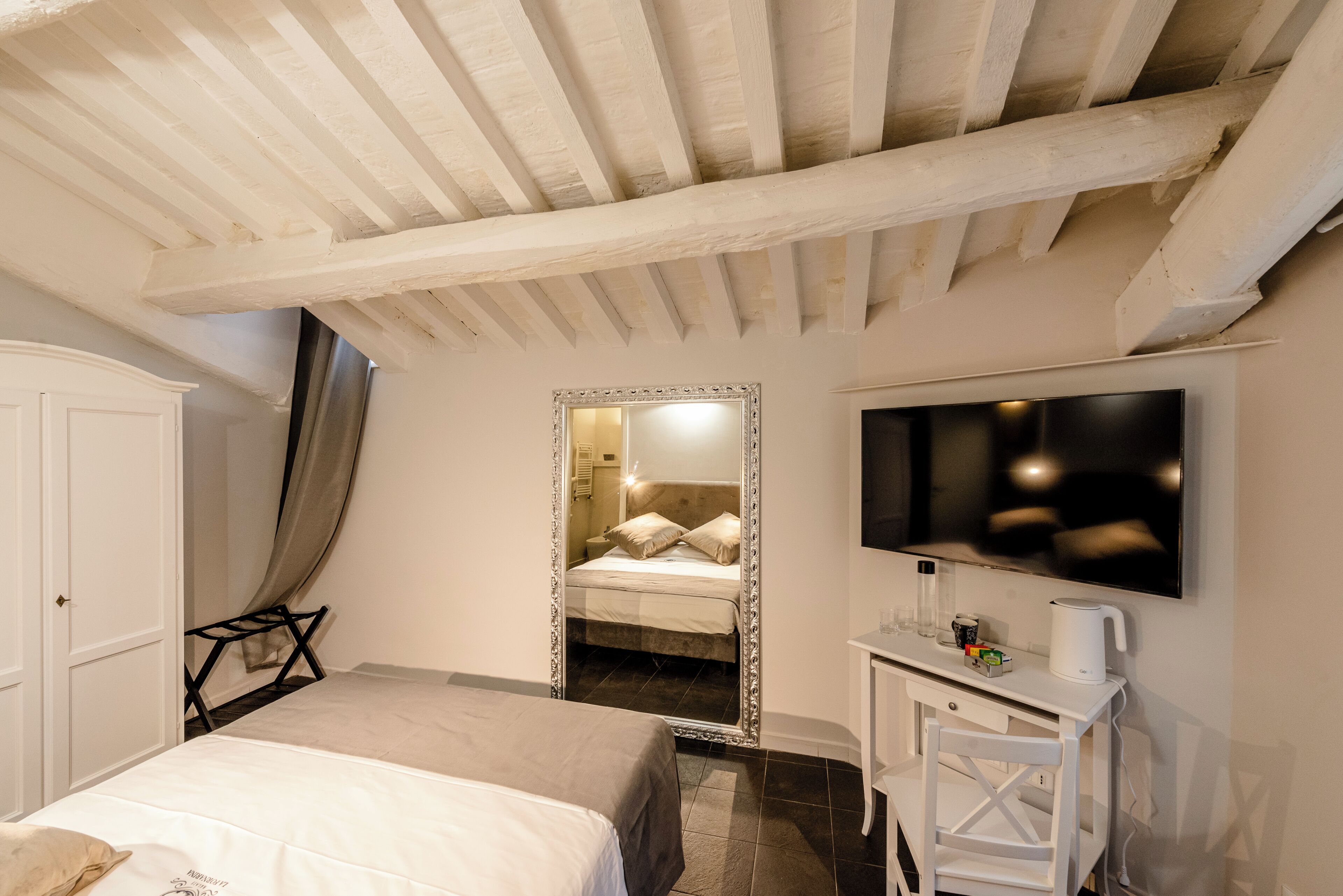 Een slaapkamer met een bed, een grote spiegel, een televisie en een bureau met een waterkoker.