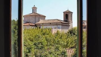 Visão pela janela de um edifício com uma torre de sino e uma cúpula, rodeado de vegetação.