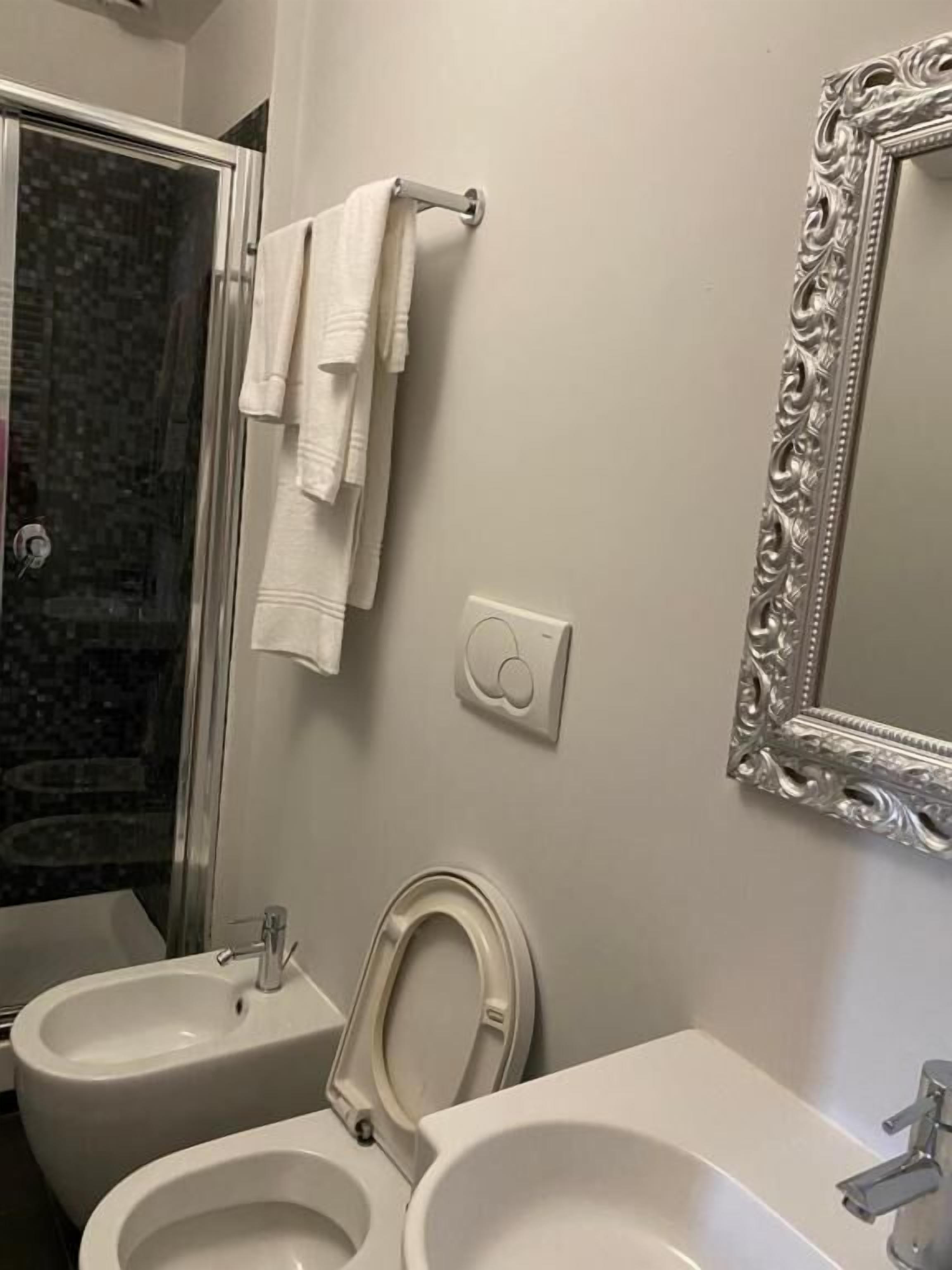 Une salle de bain équipée d’un bidet, de toilettes, d’un lavabo et d’un miroir orné d’un cadre travaillé.