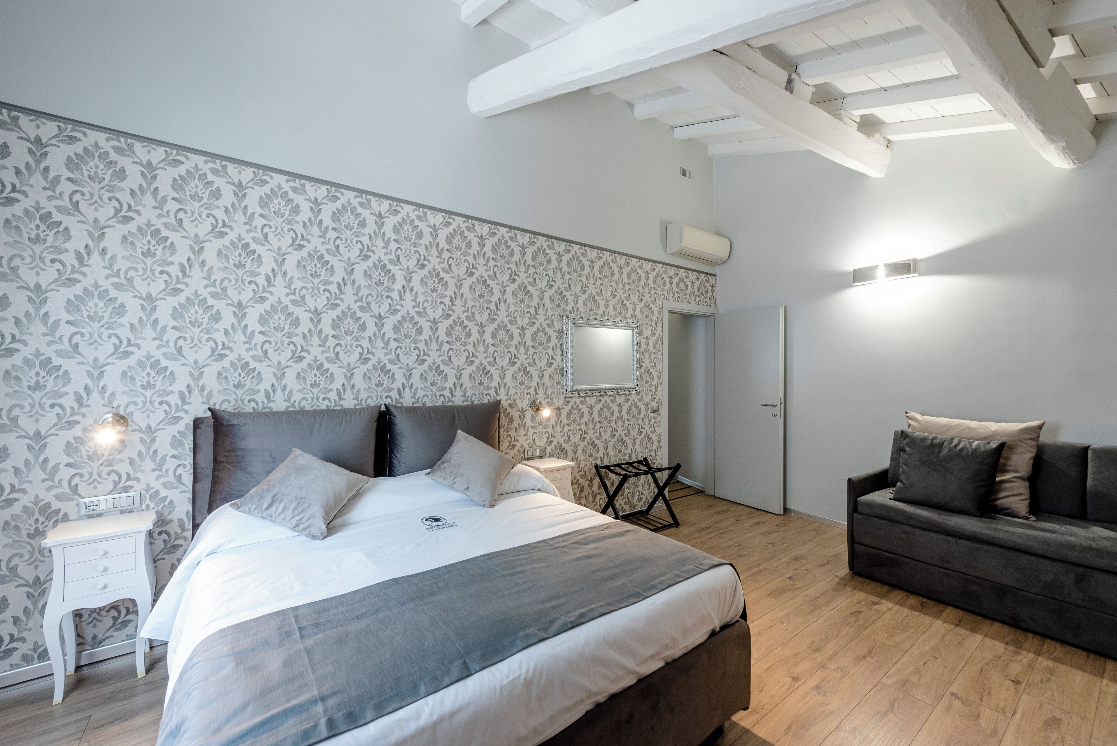 Un dormitorio con una cama grande, una mesita de noche, un aparador, un sofá y un espejo.