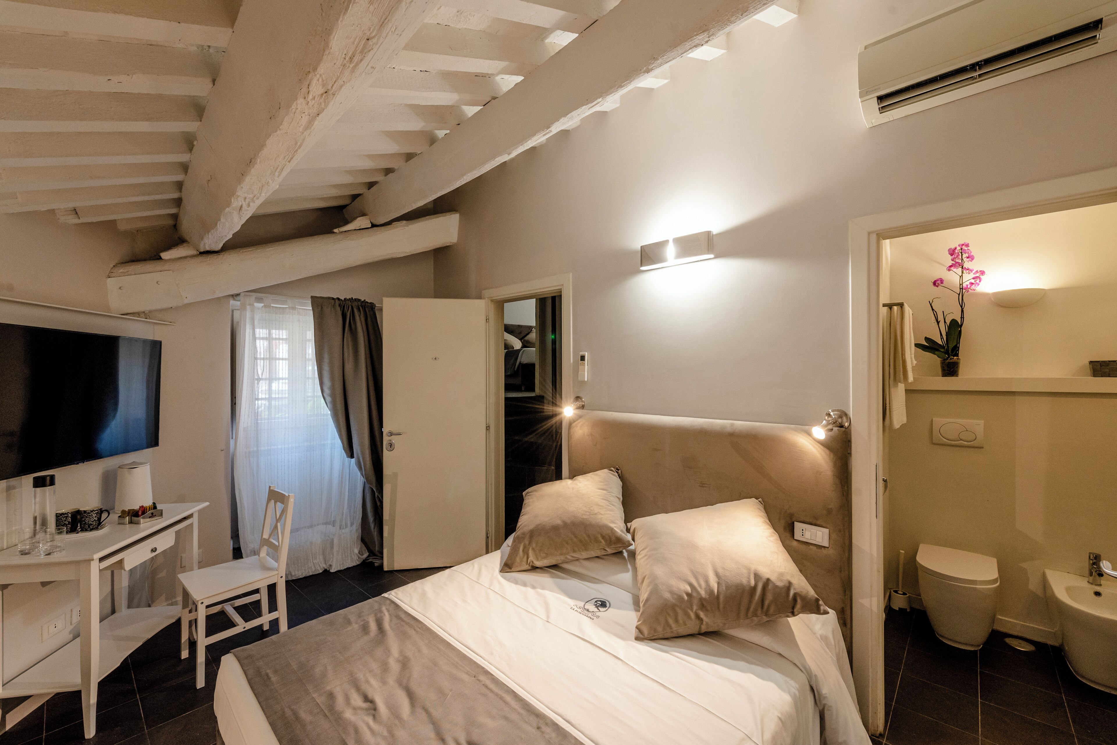 Una habitación de hotel con cama, escritorio, silla, televisor y baño.