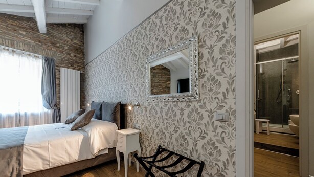 A bedroom with a bed, bedside table, mirror, and a view into the bathroom. - Fornarina a Trastevere by Welcome In (Rome)
