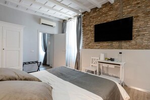 Habitación de hotel con cama, escritorio, televisor montado en una pared de ladrillo y unidad de aire acondicionado.