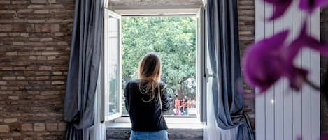 A room with a bed, a window with curtains, and a view of greenery outside.