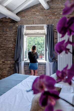 Una habitació amb un llit, una finestra amb cortines i vistes a la vegetació.
