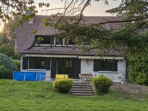 Ein zweistöckiges Haus mit einem geneigten Dach, einer Veranda mit einer Bank und einer kleinen Treppe, die zum Eingang führt.