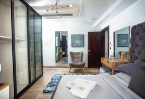A modern bedroom with a bed, a chair, a desk, and a large mirror. - Eko Atlantic Apartment (Lagos)