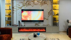 A modern living room with a flat-screen TV, a fireplace, and marble wall panels. - Eko Atlantic Apartment (Lagos)