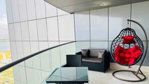 A balcony with a glass table, wicker furniture, and a red hanging chair. - Eko Atlantic Apartment (Lagos)