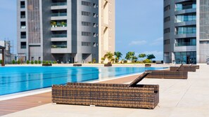 A swimming pool with wicker loungers and modern buildings in the background. - Eko Atlantic Apartment (Lagos)