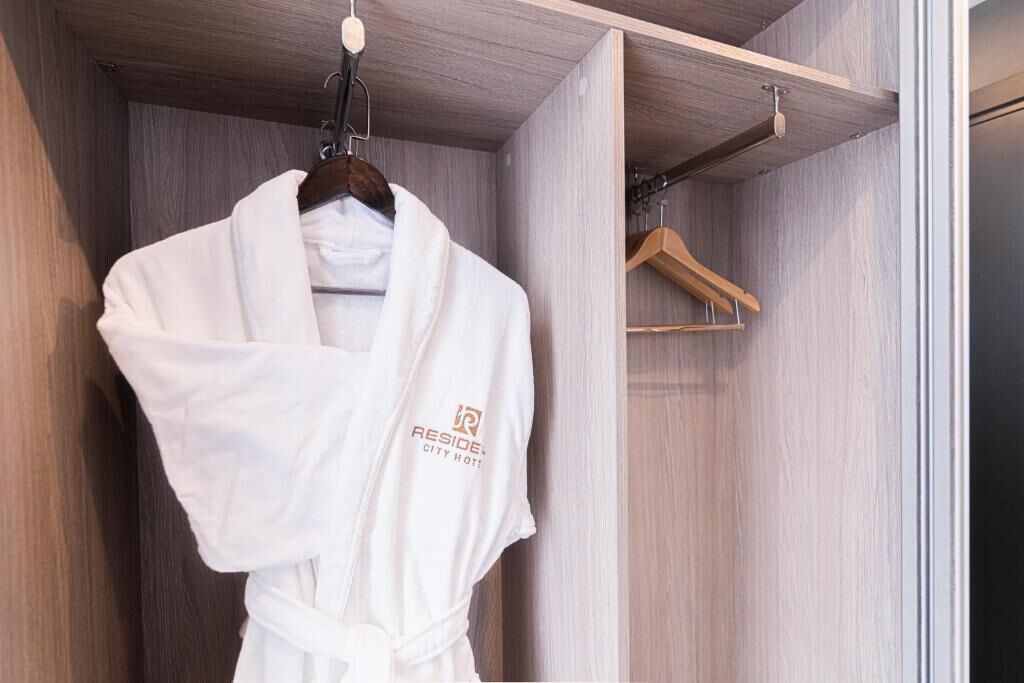 A white robe hanging in a wooden closet with a wooden hanger and a wooden hanger rod.