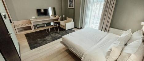 A hotel room with a bed, a desk, a chair, a television, and a window with curtains.