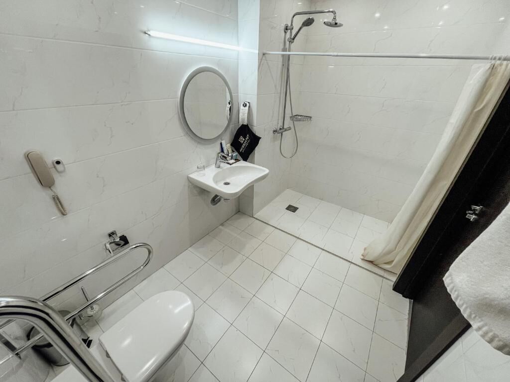 A modern bathroom with a toilet, sink, shower, and grab bars.