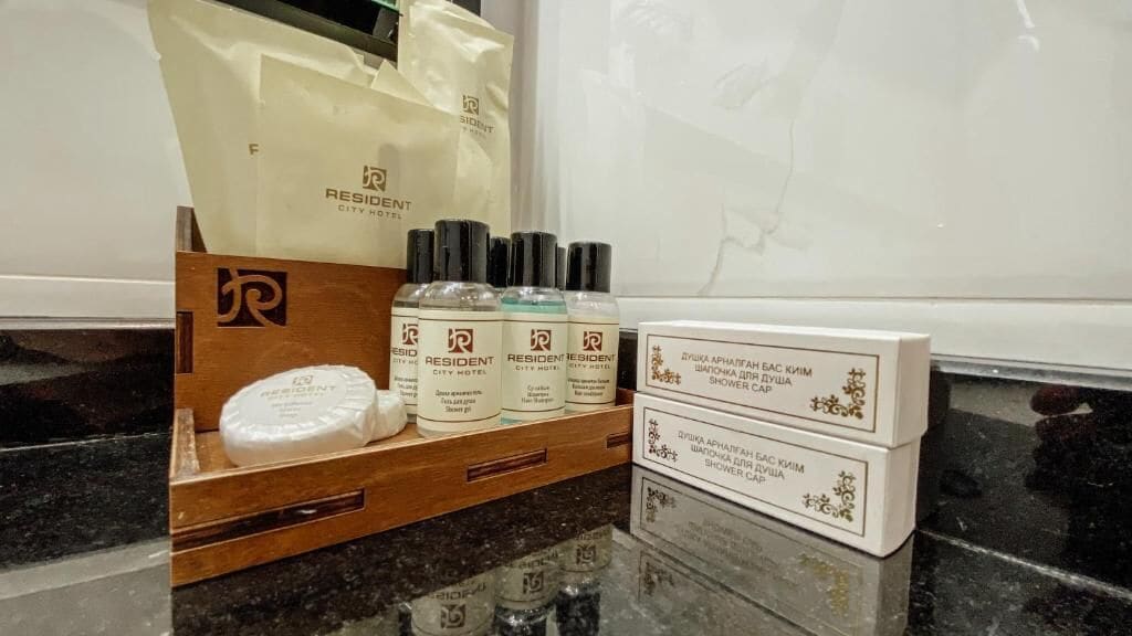 A hotel room with a wooden sideboard displaying toiletries and a Resident City Hotel branded bag.