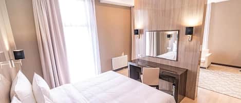 A hotel room with a bed, a desk, a mirror, and a window with curtains.