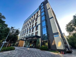 Um moderno edifício de hotel com fachada de vidro, entrada imponente e uma placa indicando ser um hotel urbano.