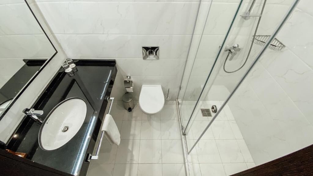 A modern bathroom with a glass shower enclosure, a white toilet, and a black countertop with a sink.