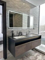 A modern bathroom with a large mirror, dual sinks, and a view of the city.