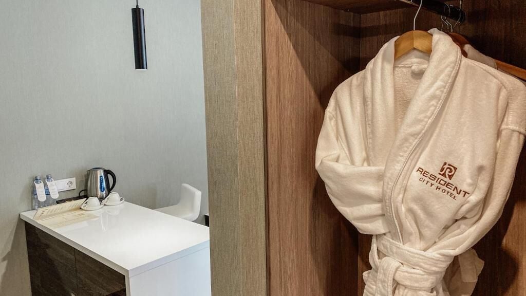 A bathroom with a white sink, a kettle, and a robe hanging on a wooden door.