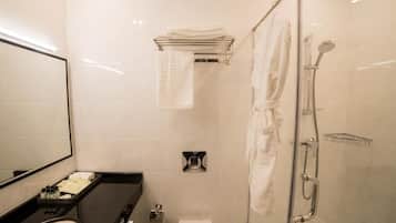 A modern bathroom with a glass shower enclosure, a black countertop with toiletries, and a white towel rack.