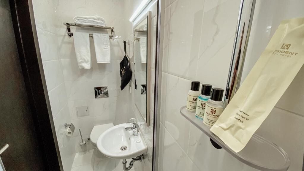 Un bany modern amb dutxa de vidre, un lavabo blanc i un escurapulides.