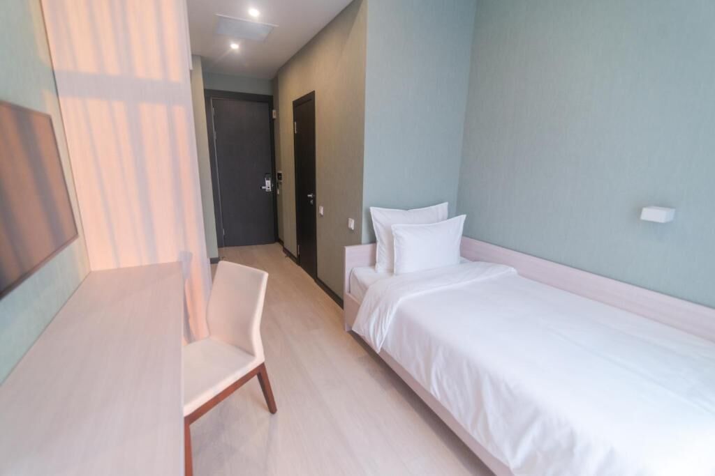 A hotel room with a bed, a chair, a door, and a light-colored floor.