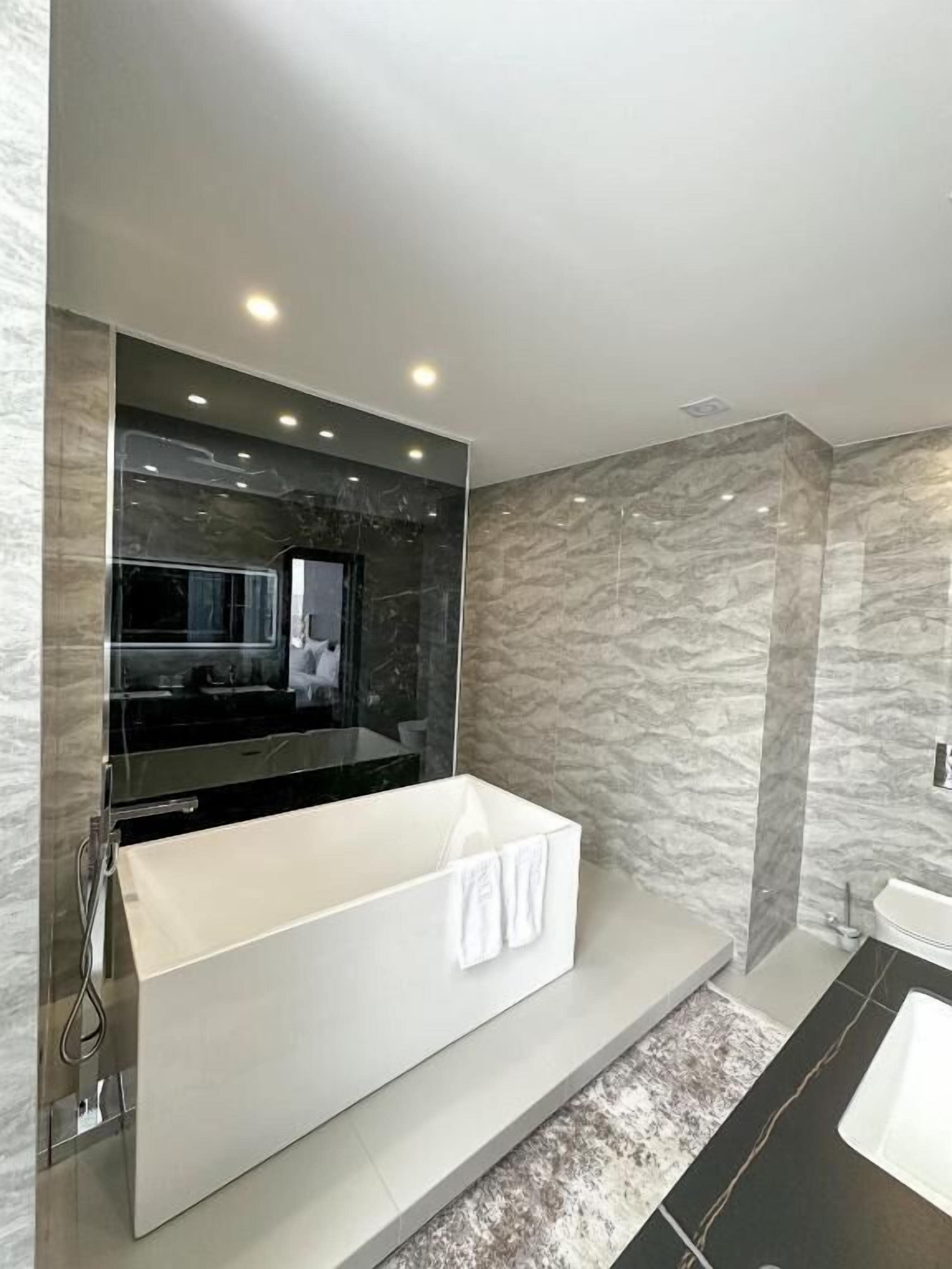 A modern bathroom with a large mirror, a white bathtub, and marble walls.