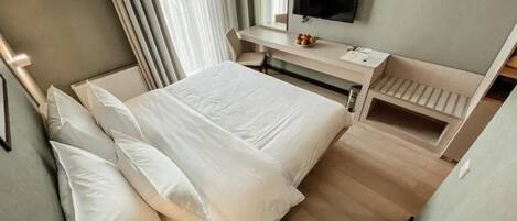 Una habitación de hotel con cama, escritorio, televisor y ventana con cortinas.