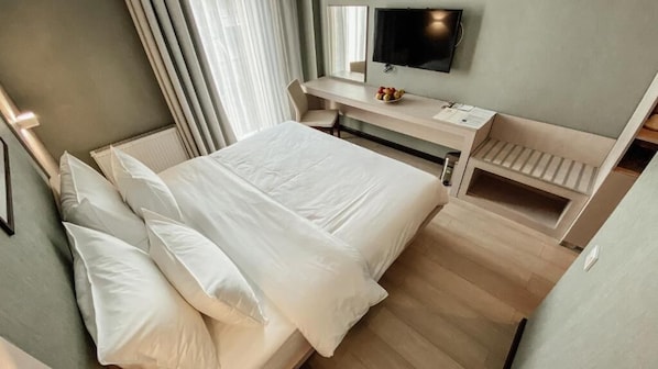 Una habitación de hotel con cama, escritorio, televisor y ventana con cortinas.