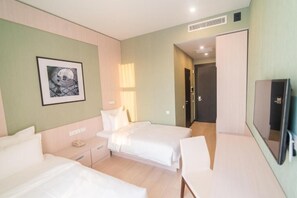 Habitación de hotel con dos camas, un escritorio, una silla, un televisor y un cuadro en la pared.
