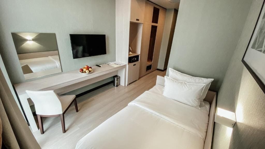 A hotel room with a bed, a desk with a chair, a television, and a wardrobe.