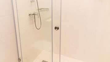 Ducha envuelta en vidrio con cabezal de ducha de mano, puerta de cristal y suelo de baldosas blancas.