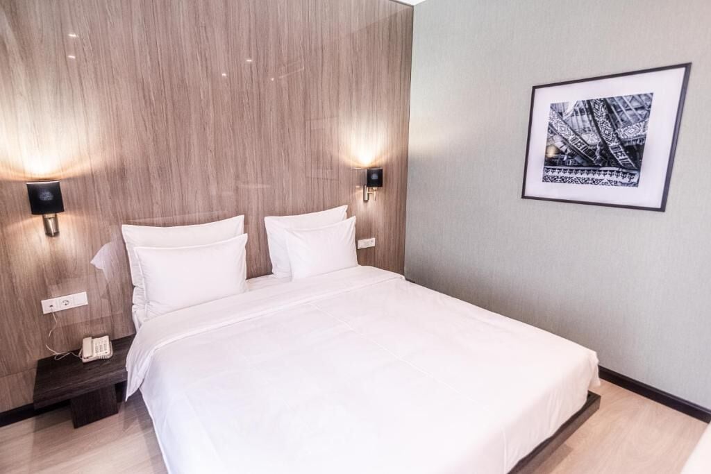 A hotel room with a large bed, two bedside lamps, a telephone, and a framed picture on the wall.