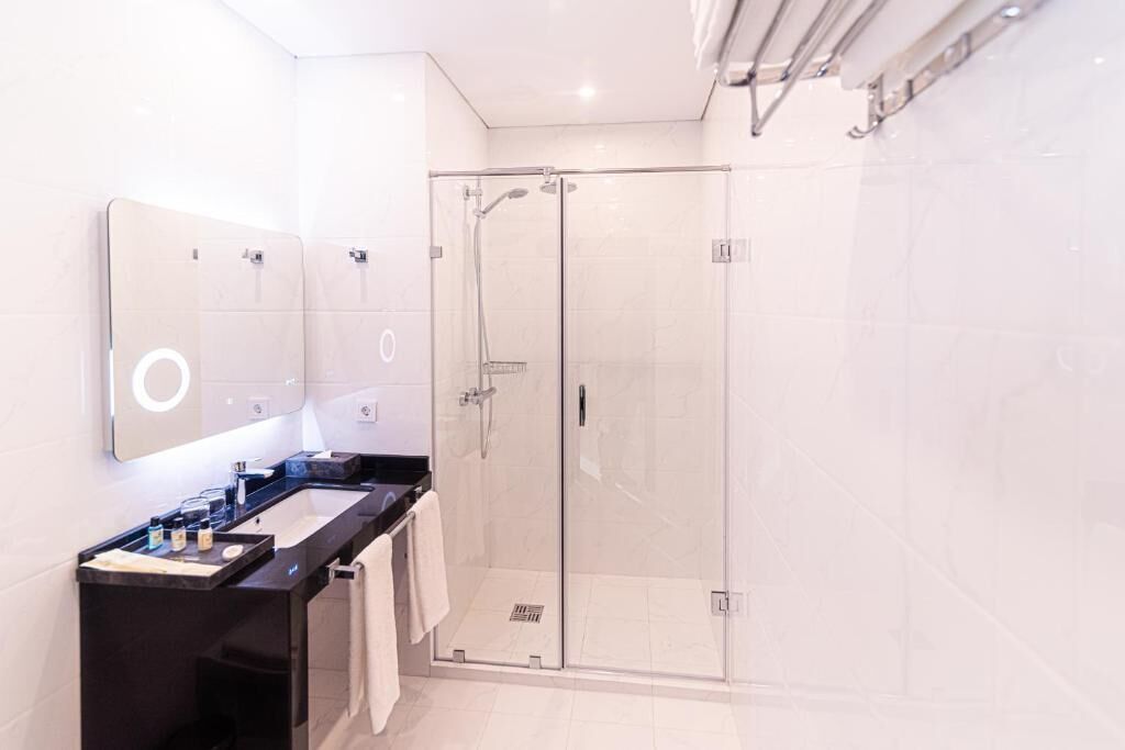 A modern bathroom with a glass-enclosed shower, a black vanity with a mirror, and a white tiled floor.