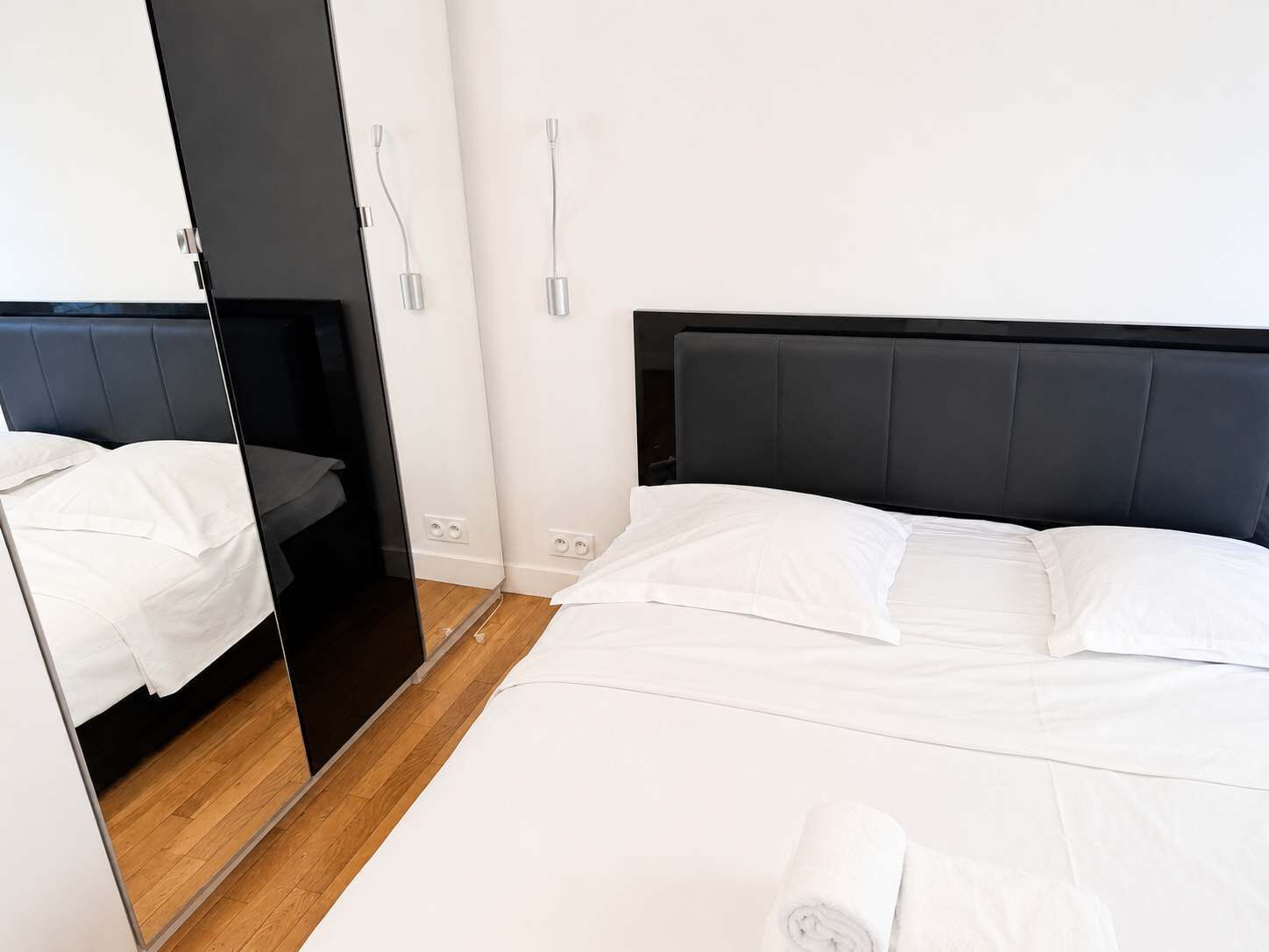 A modern hotel room with a large bed, a wardrobe, and a mirror.