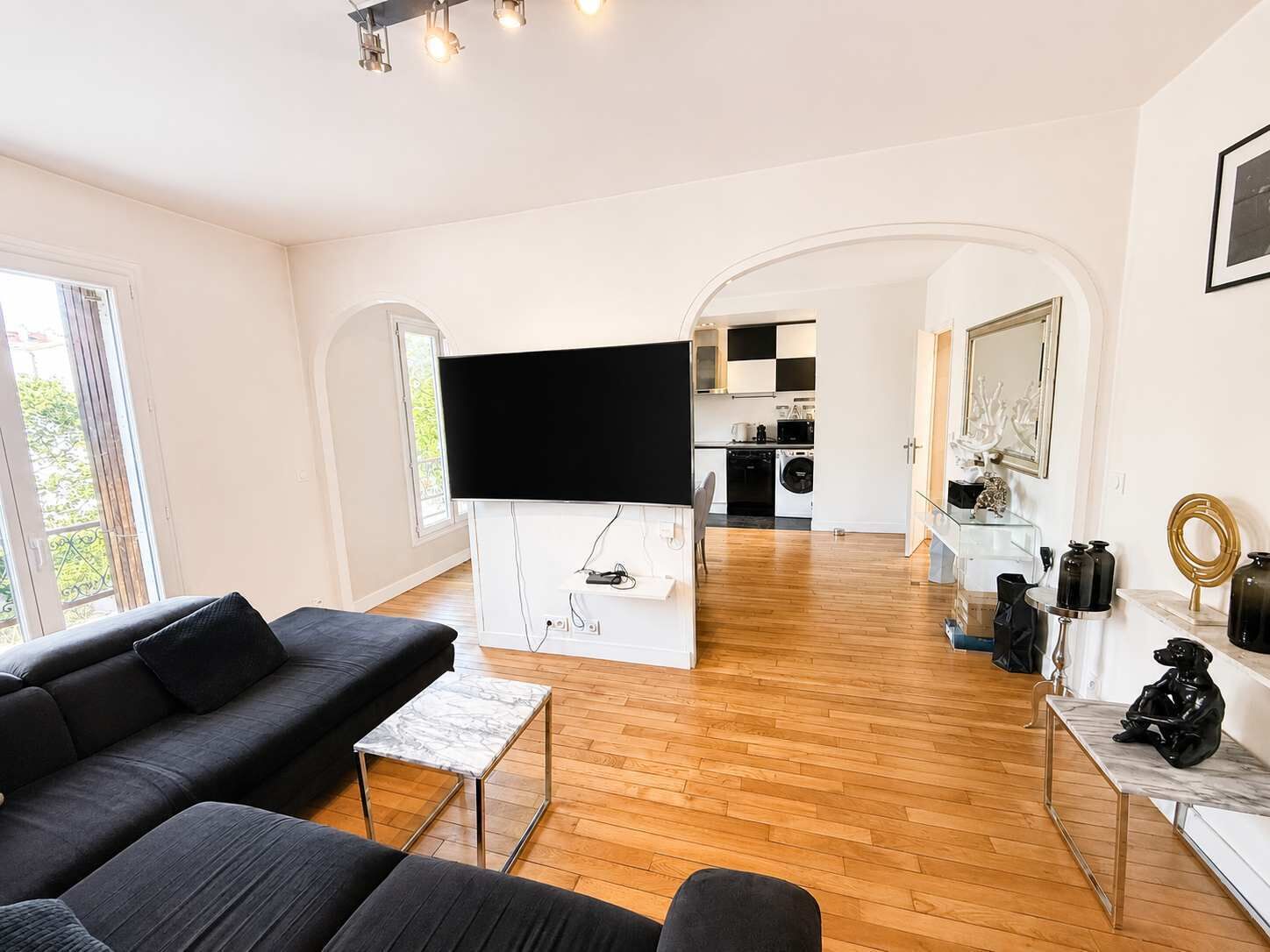 Un salon moderne avec un canapé noir, une table basse en marbre et un téléviseur à écran plat fixé à un mur blanc.