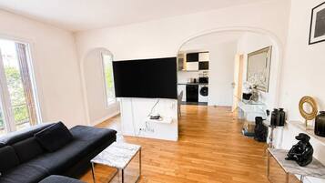 A modern living room with a black sofa, a marble coffee table, and a flat-screen TV mounted on a white wall.