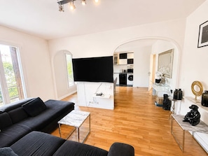 Una sala de estar moderna con un sofá negro, una mesa de centro de mármol y un televisor de pantalla plana montado en una pared blanca.
