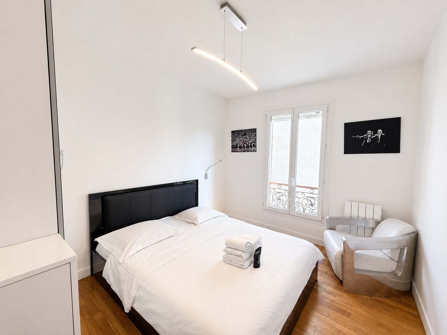 Un dormitorio con cama, una silla, un ventanal con vistas y un cuadro colgado en la pared.