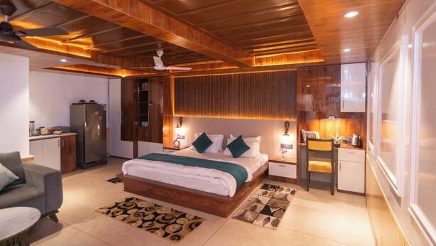 Un dormitorio moderno con techo de madera, una cama grande con una manta verde, un escritorio pequeño y un refrigerador.