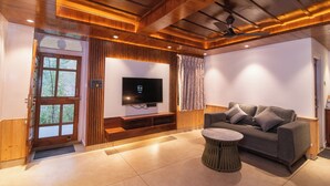 Una sala de estar moderna con un televisor de pantalla plana, un sofá gris, una mesa de centro redonda, vigas de madera en el techo y una puerta con ventanal.