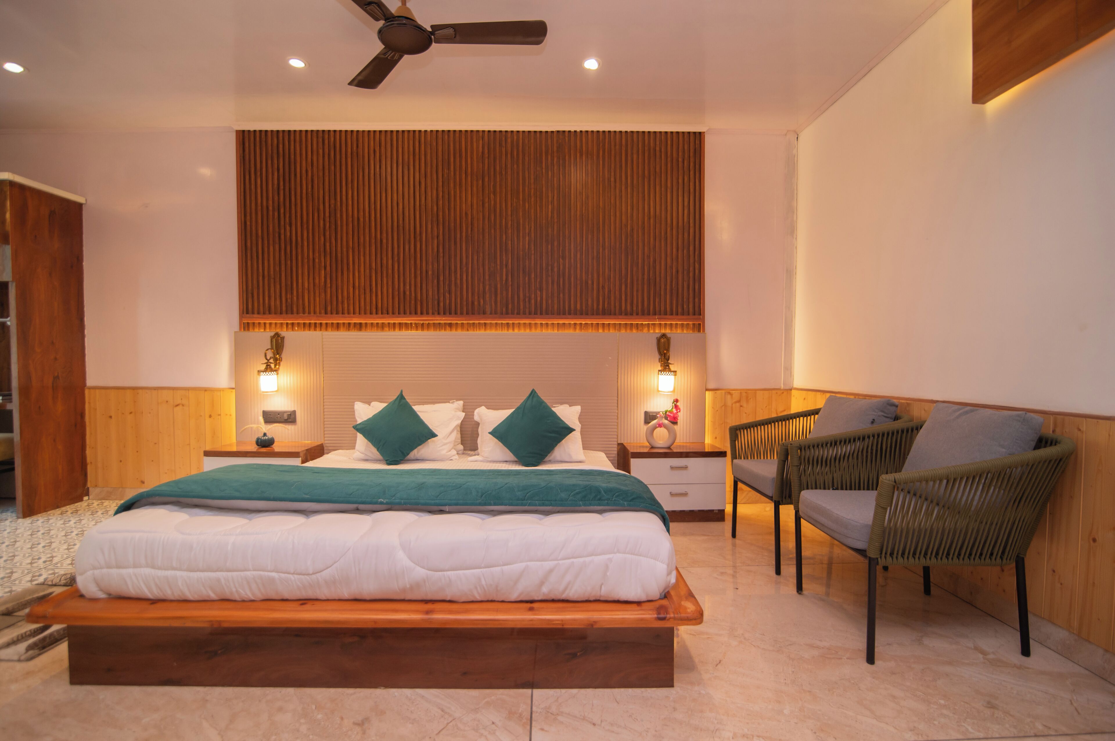 Un dormitorio con una cama de madera, dos mesitas de noche con lámparas, un ventilador de techo y una silla de mimbre.